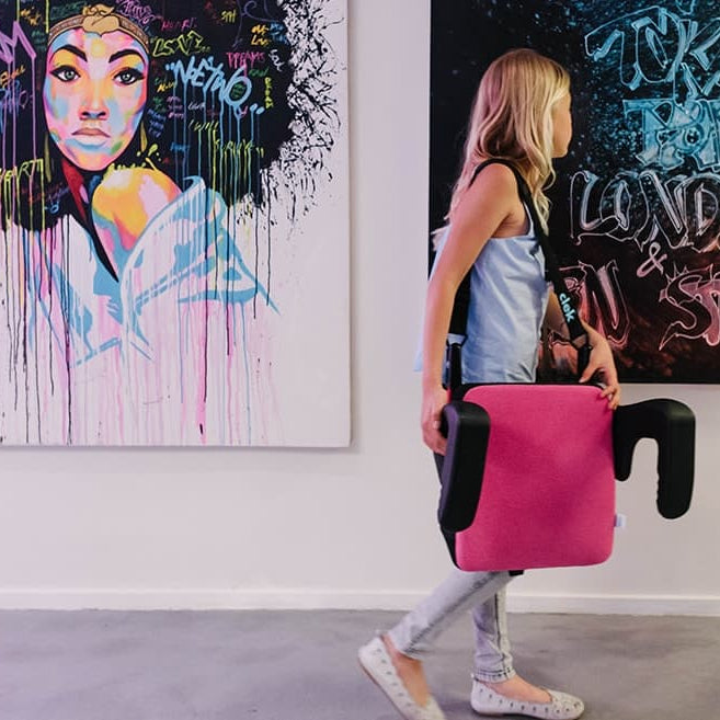 Girl carrying her Clek Olli Booster Seat using the strap-thingy accessory