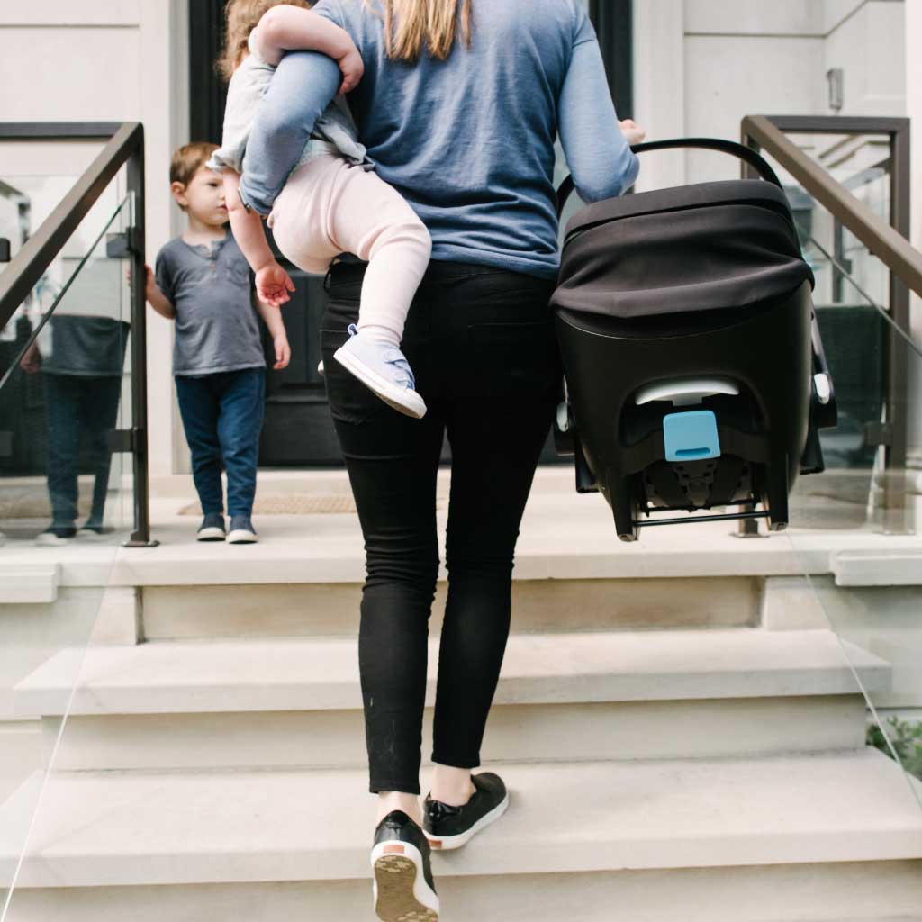 Mom carrying her baby and a Clek Liing infant car seat