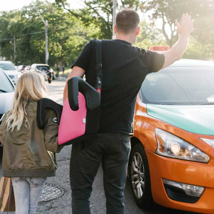 Dad carrying his daughter's Clek Olli booster seat while hailing a taxi cab