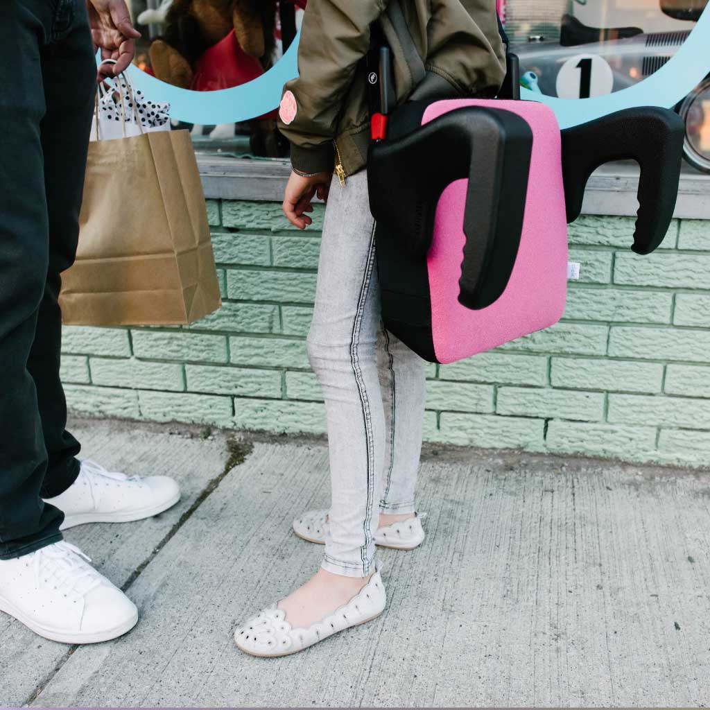 Girl carrying her Clek Olli booster seat outside of a shop