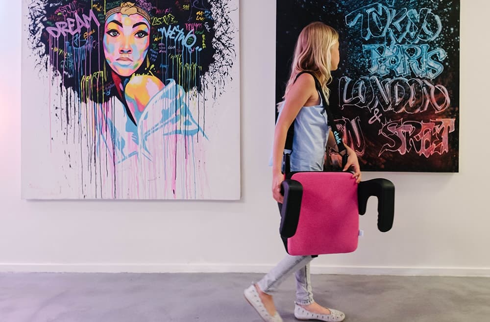 Girl carrying her Clek Olli Booster Seat using the strap-thingy accessory