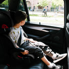 Child sitting in a car seat inside a vehicle with a view of an outdoor scene through the window. all-groups